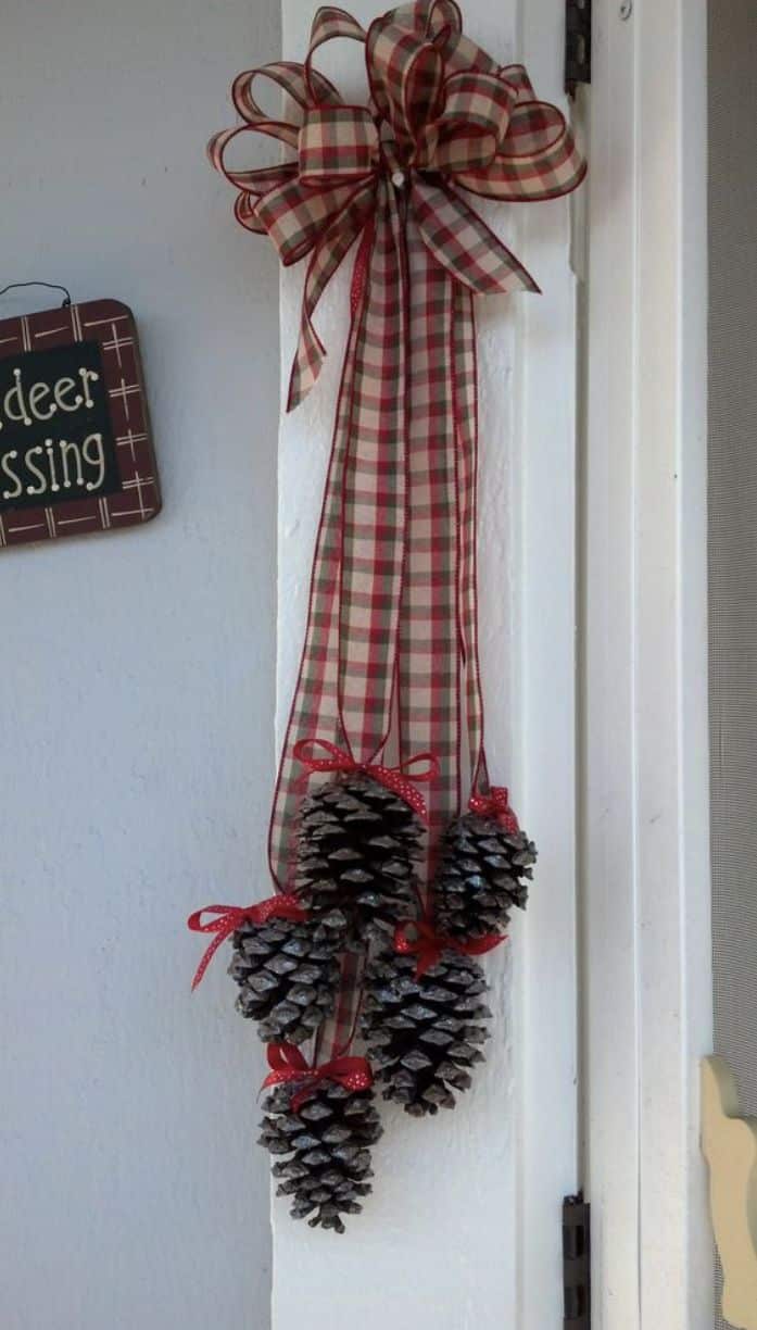 Cluster of pinecones hanging from a red and green plaid ribbon bow on a white door frame