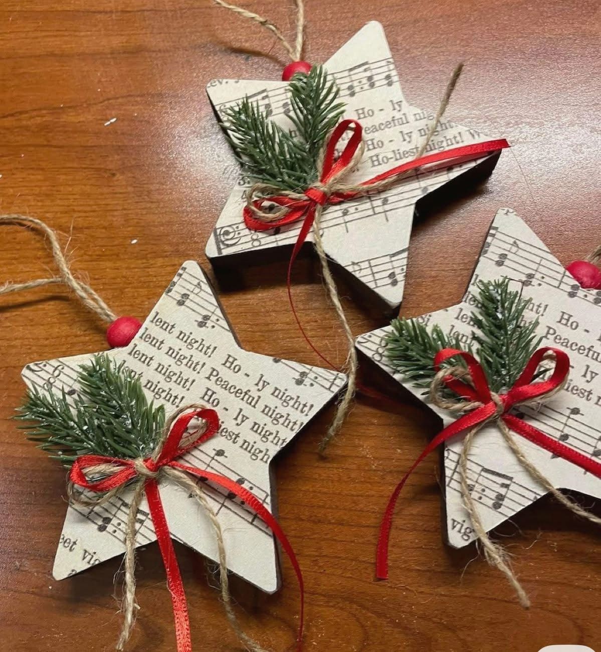 Wooden star ornaments covered in Christmas carol sheet music with faux pine, red ribbon and twine bows