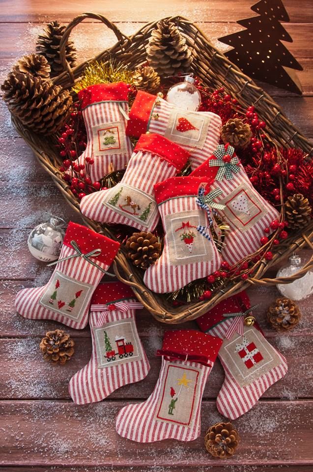 Mini red and white striped Christmas stockings with cross stitch motifs in a wicker basket with pinecones