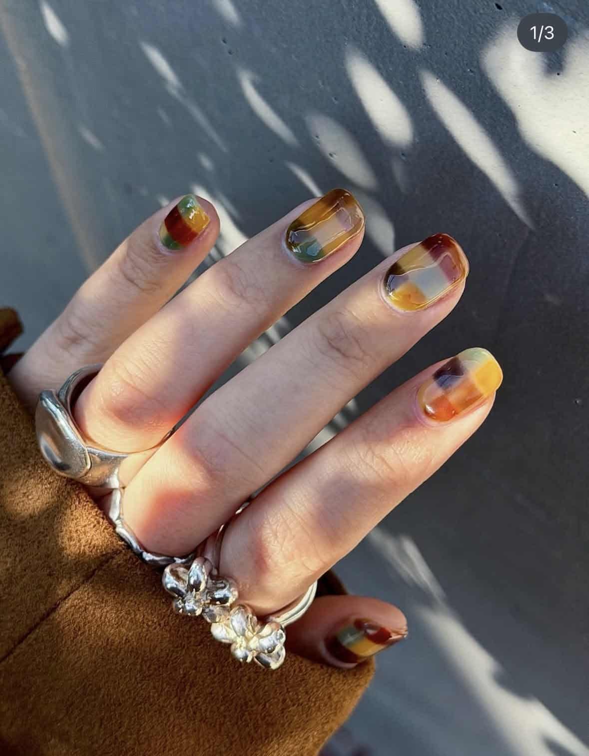 Short squoval nails with translucent amber, olive and cranberry patchwork jelly design
