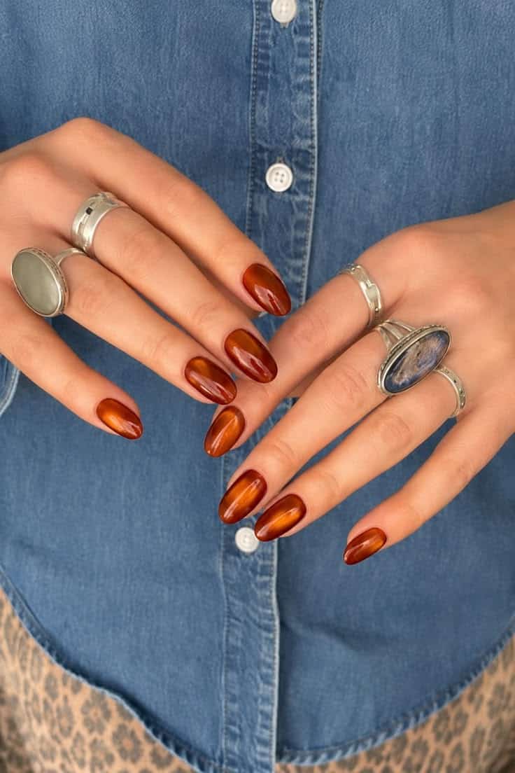 Almond nails in a burnt orange cat eye finish with silver rings