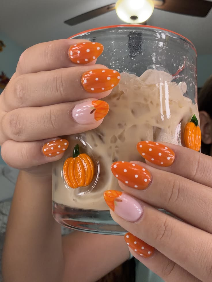 Almond nails with orange and white polka dots and pink accent nails with orange pumpkin tips