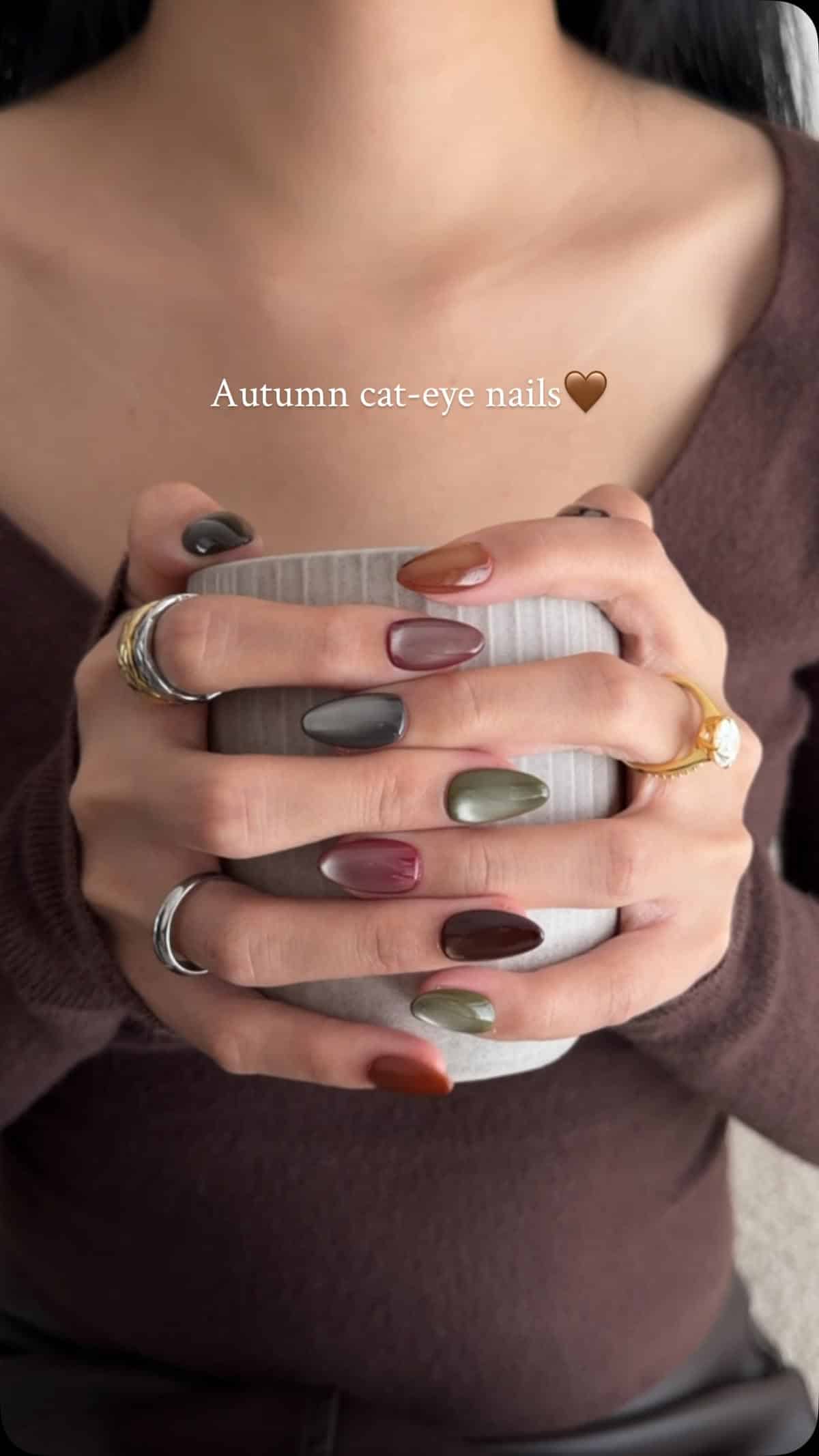Almond cat eye nails in sage, charcoal, plum, rust and chocolate brown holding a mug